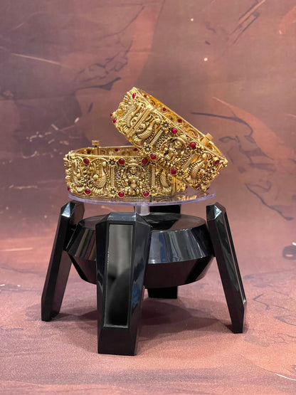 Gold bracelet with red stones on a black stand against a brown background