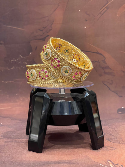 Gold bangles with gemstones on a black stand against a brown background