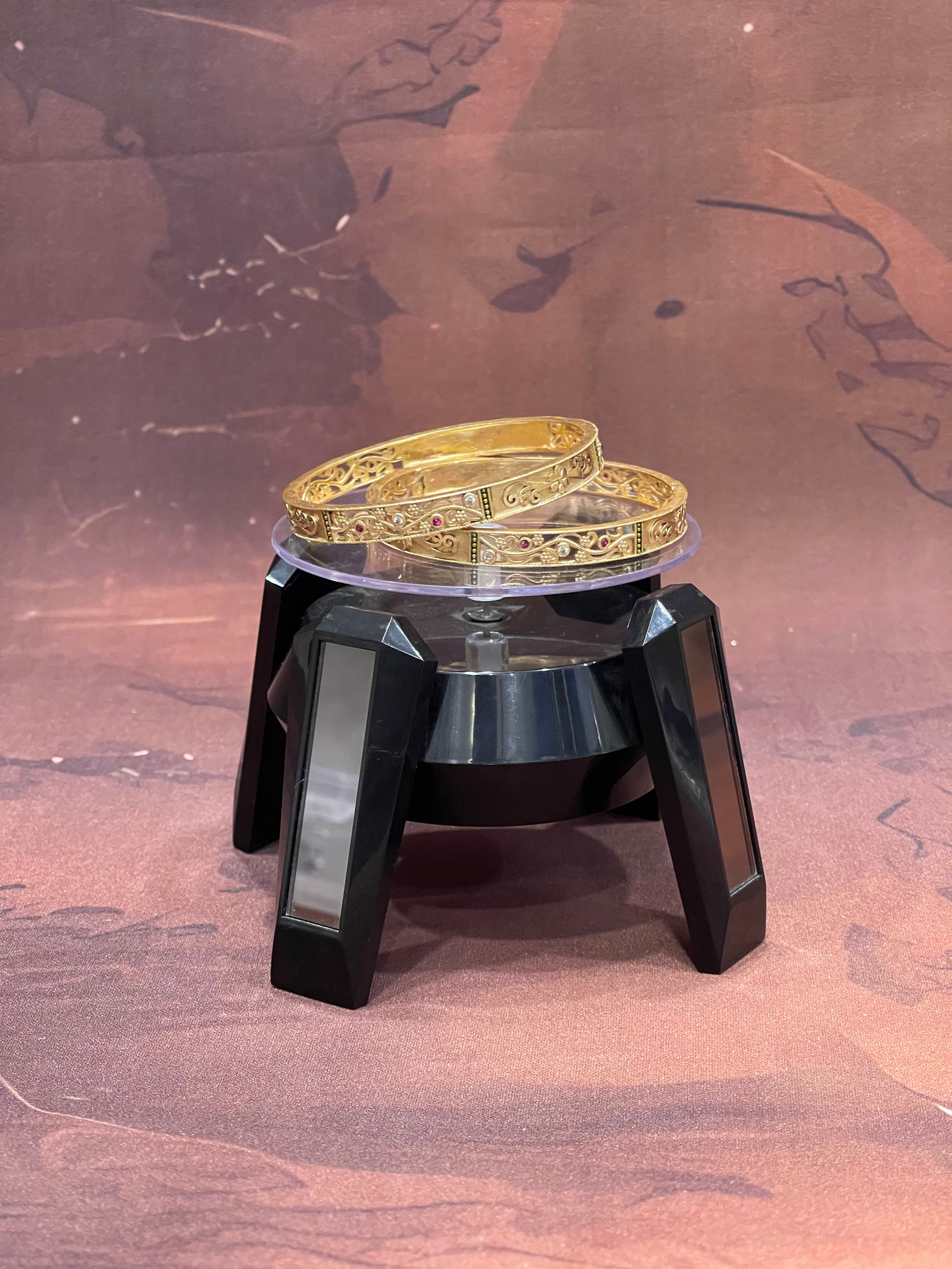 Gold bracelet on a black and silver stand against a brown background