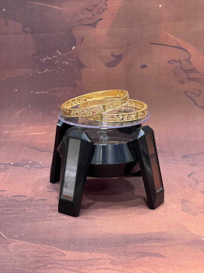 Gold bracelet on a black and silver stand against a brown background